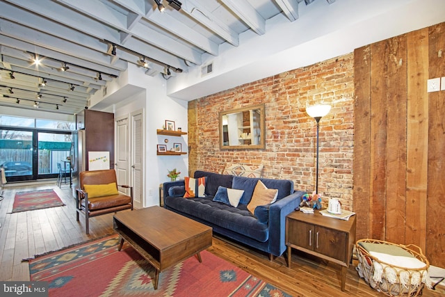 living room with track lighting, brick wall, visible vents, hardwood / wood-style floors, and beam ceiling