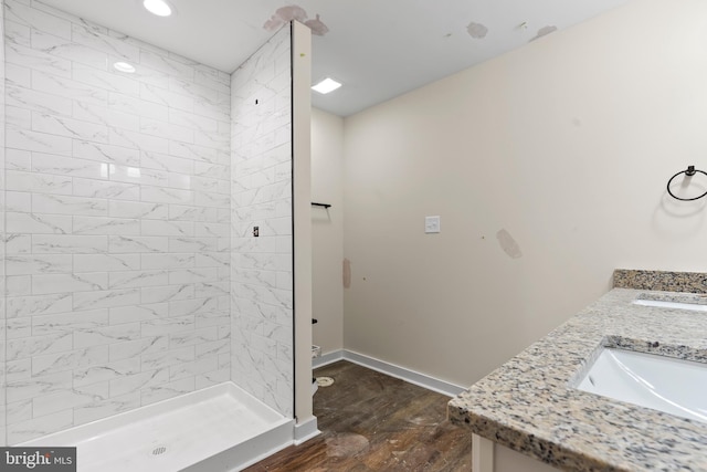 full bathroom featuring double vanity, a stall shower, a sink, wood finished floors, and baseboards