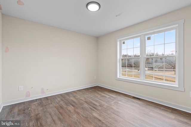 spare room with baseboards, visible vents, and wood finished floors