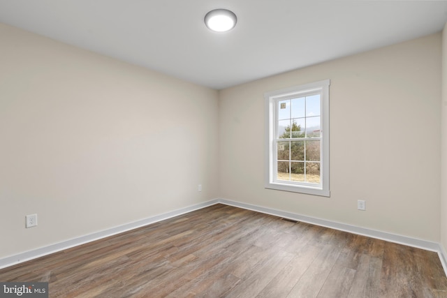 empty room featuring wood finished floors, visible vents, and baseboards