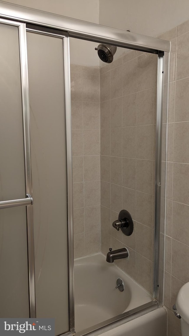 full bath featuring toilet and shower / bath combination with glass door