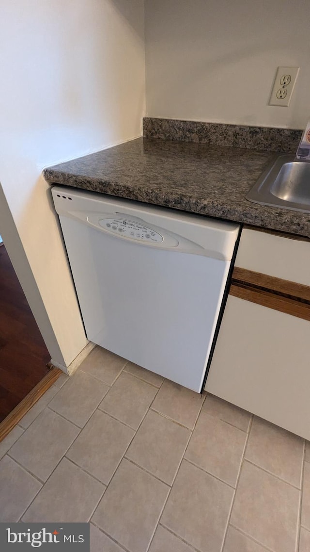 kitchen featuring light tile patterned floors, dark countertops, white dishwasher, white cabinetry, and a sink