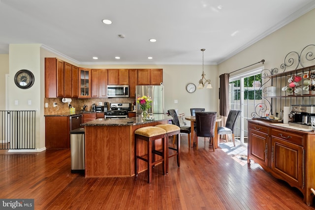 kitchen with dark wood-style floors, a kitchen island, appliances with stainless steel finishes, a kitchen bar, and backsplash