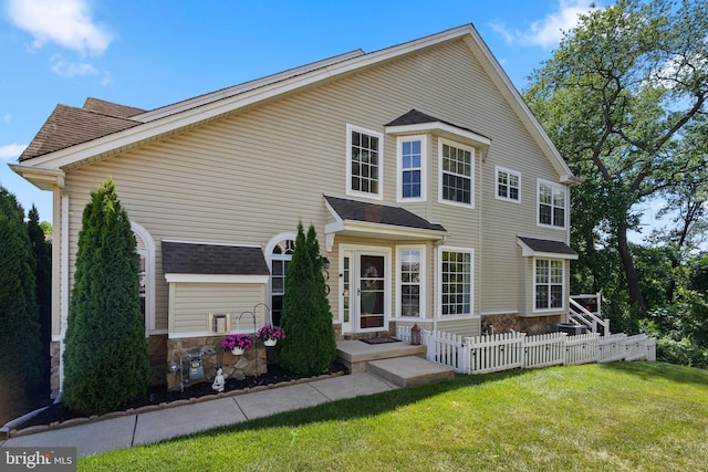 view of front facade with roof with shingles, fence, and a front lawn