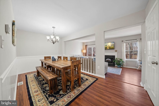 dining space with visible vents, baseboards, a fireplace, wood finished floors, and a notable chandelier