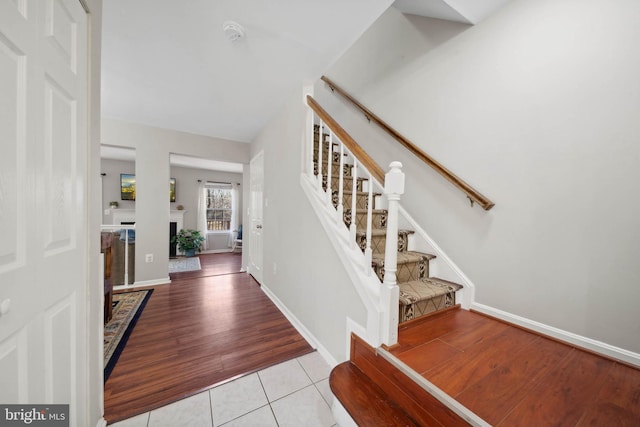 foyer entrance featuring tile patterned floors, a fireplace, stairs, and baseboards