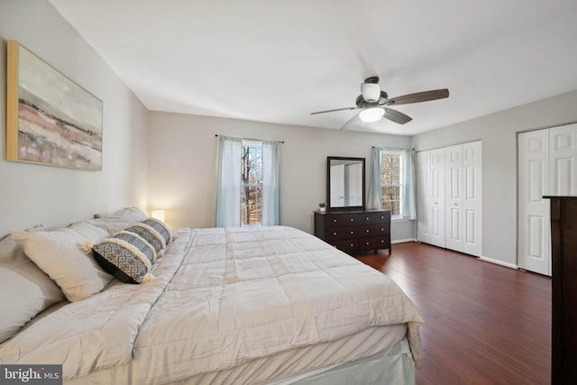 bedroom with two closets, dark wood-type flooring, baseboards, and a ceiling fan