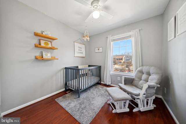 bedroom featuring baseboards, a nursery area, wood finished floors, and a ceiling fan