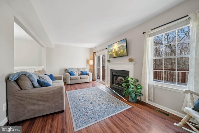 living area with visible vents, baseboards, wood finished floors, and a fireplace with flush hearth