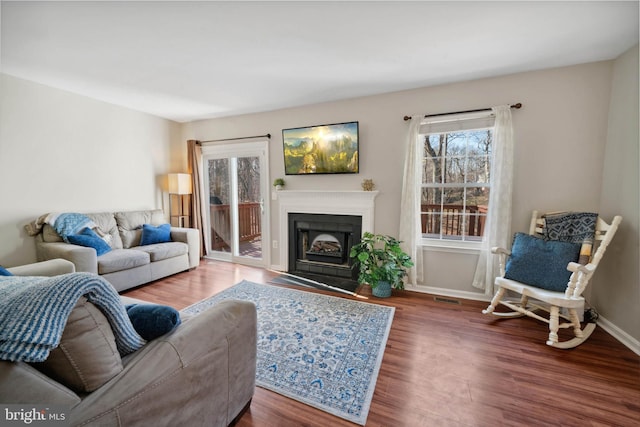 living area featuring a fireplace with flush hearth, visible vents, baseboards, and wood finished floors