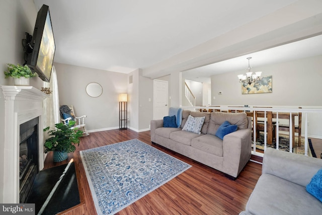 living area with a notable chandelier, a fireplace with raised hearth, wood finished floors, baseboards, and stairs