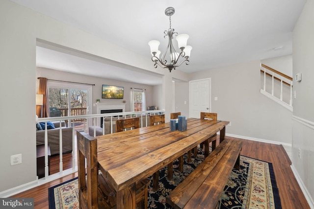 dining room with baseboards, stairs, a fireplace, an inviting chandelier, and wood finished floors