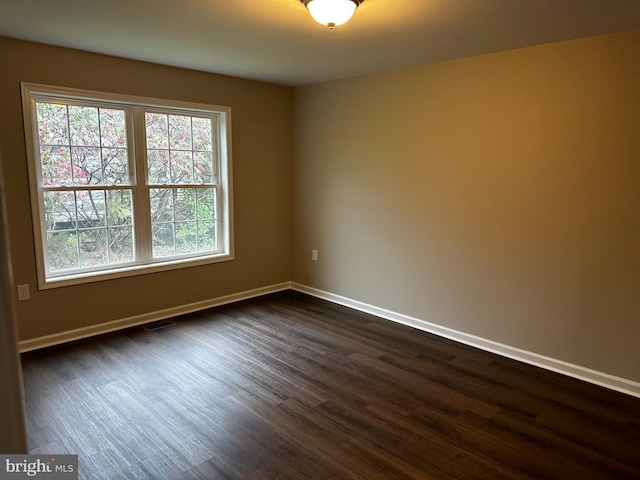 unfurnished room featuring dark wood-style floors, baseboards, and visible vents