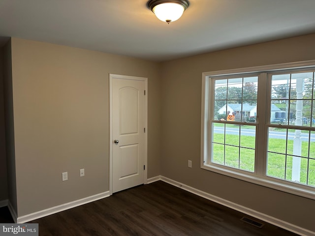 empty room with baseboards, visible vents, and dark wood-type flooring