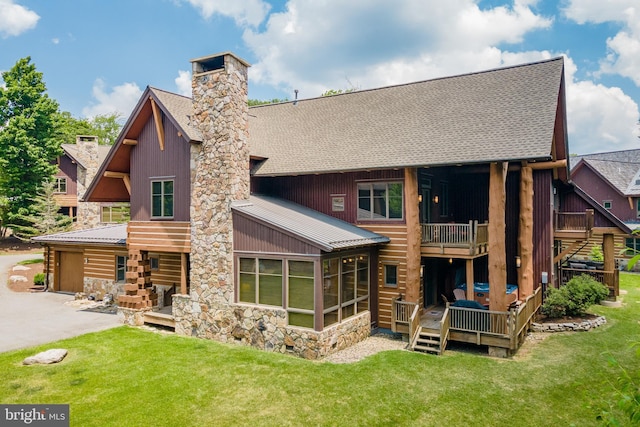 back of property featuring a chimney, a garage, a yard, a deck, and stone siding