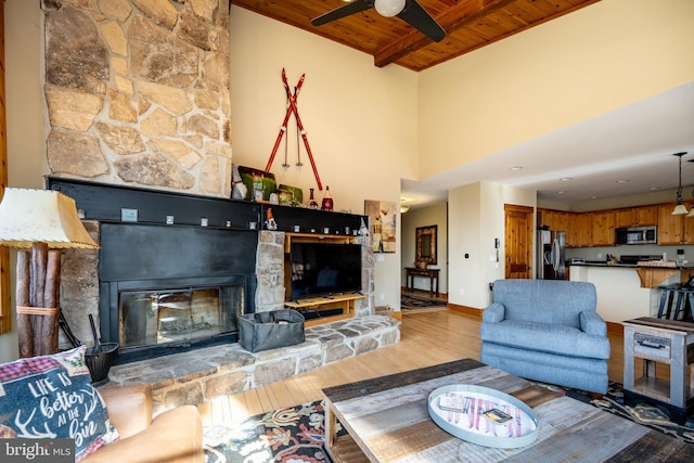 living area featuring baseboards, a fireplace, light wood-style floors, wooden ceiling, and beamed ceiling