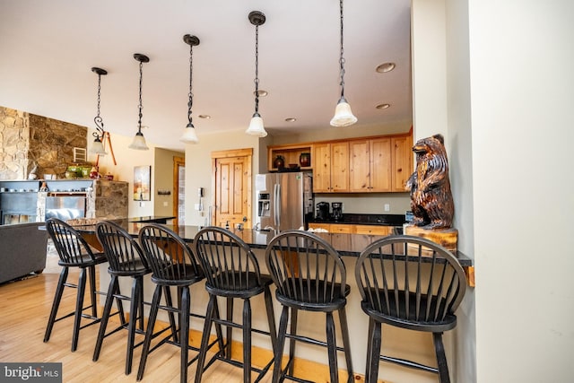 kitchen with dark countertops, a breakfast bar area, stainless steel fridge with ice dispenser, and light wood finished floors