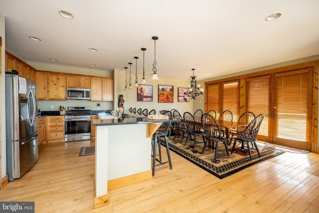 kitchen with a kitchen bar, a notable chandelier, dark countertops, light wood-style floors, and appliances with stainless steel finishes