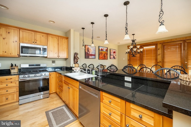 kitchen featuring light wood-type flooring, pendant lighting, a sink, dark countertops, and stainless steel appliances