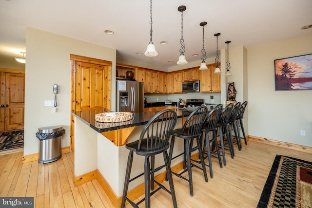 kitchen featuring light wood-type flooring, a breakfast bar, dark countertops, appliances with stainless steel finishes, and a peninsula