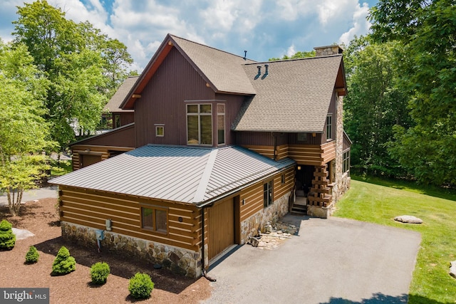 view of front of property featuring a front yard, a chimney, a garage, stone siding, and aphalt driveway