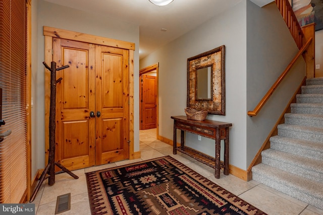 entryway with light tile patterned floors, visible vents, stairs, and baseboards