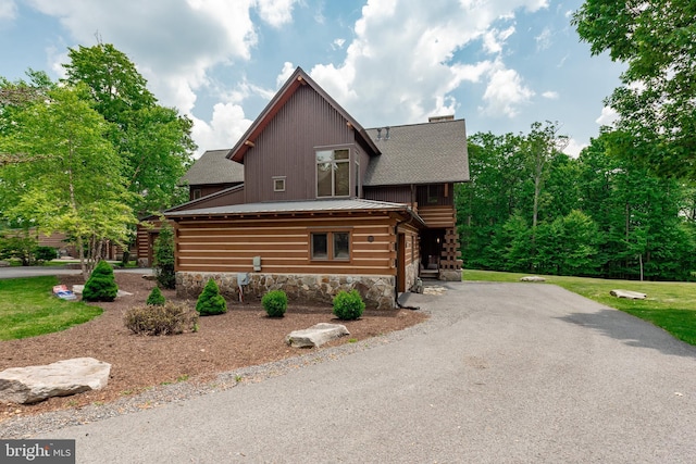 view of side of home featuring stairs, stone siding, roof with shingles, and driveway