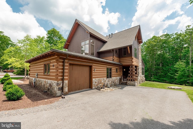 view of front of property with aphalt driveway, stone siding, and roof with shingles