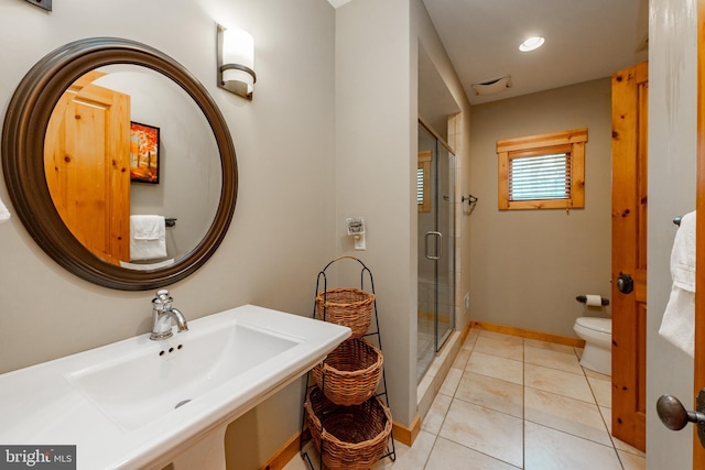 bathroom featuring toilet, a stall shower, a sink, tile patterned flooring, and baseboards