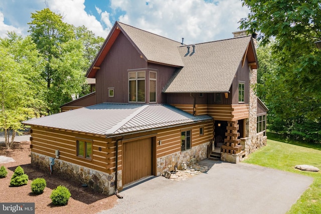 view of front facade with aphalt driveway, stone siding, a chimney, and a front yard