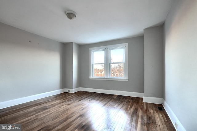 unfurnished room with dark wood-style floors, visible vents, and baseboards