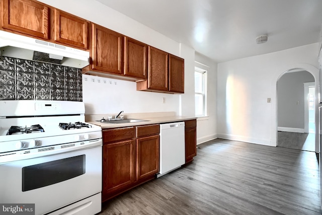 kitchen with arched walkways, under cabinet range hood, white appliances, wood finished floors, and a sink