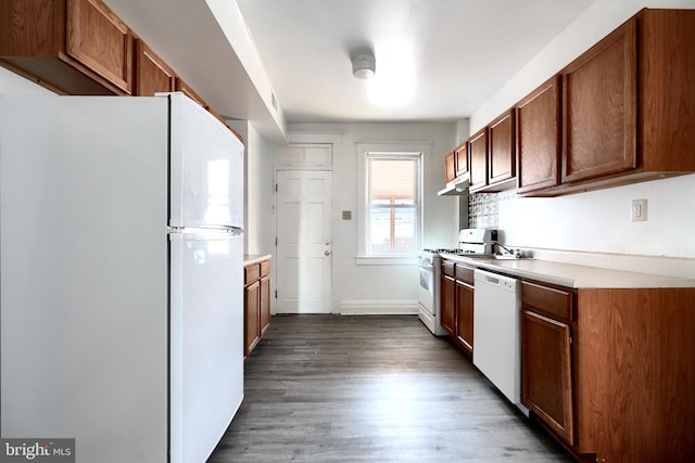 kitchen with under cabinet range hood, white appliances, wood finished floors, light countertops, and brown cabinetry