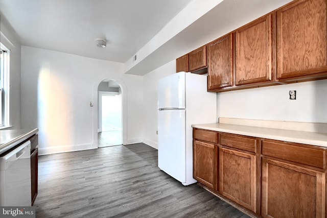 kitchen with white appliances, arched walkways, brown cabinetry, dark wood-style floors, and light countertops