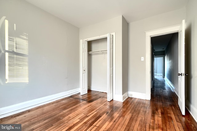 unfurnished bedroom featuring a closet, wood-type flooring, and baseboards