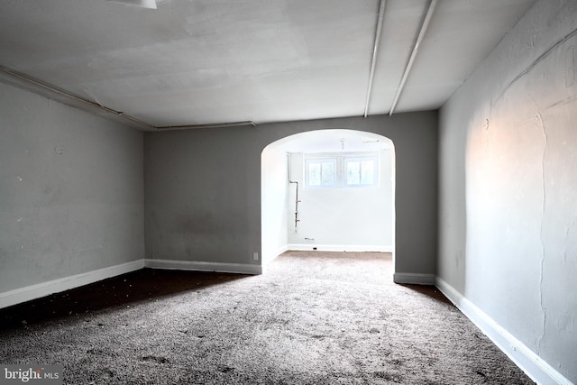 carpeted spare room featuring arched walkways and baseboards