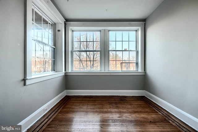 empty room featuring a healthy amount of sunlight, dark wood-style flooring, and baseboards