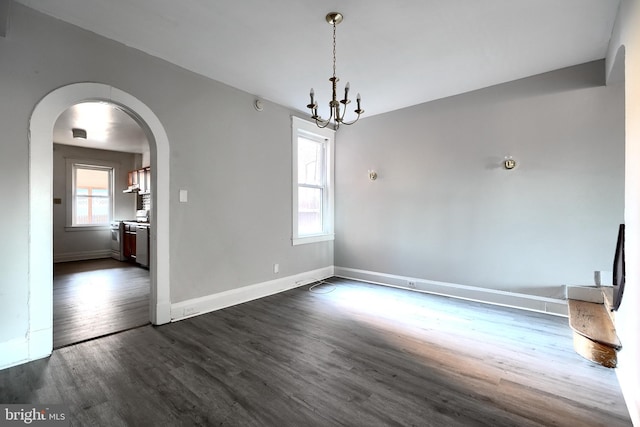 unfurnished dining area featuring an inviting chandelier, baseboards, arched walkways, and dark wood-type flooring