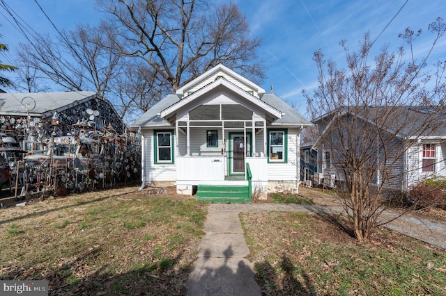 bungalow with a front lawn, a shingled roof, and a sunroom