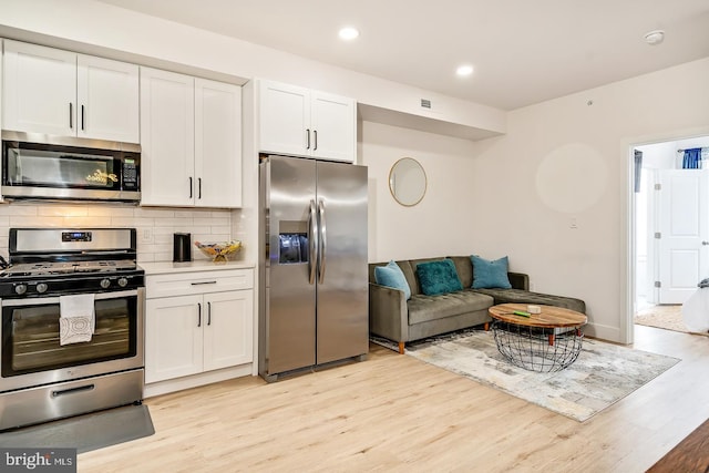 kitchen with light wood-type flooring, appliances with stainless steel finishes, decorative backsplash, and white cabinets