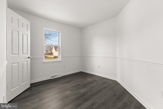 spare room featuring baseboards, visible vents, and dark wood-style flooring