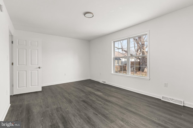 empty room featuring dark wood-type flooring, visible vents, and baseboards