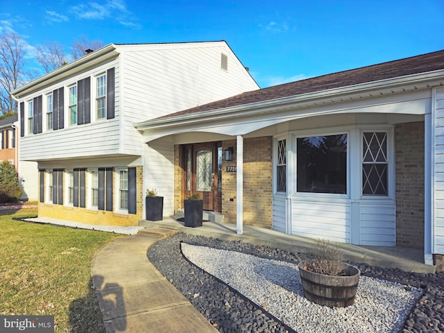 back of house with a porch, brick siding, and a yard