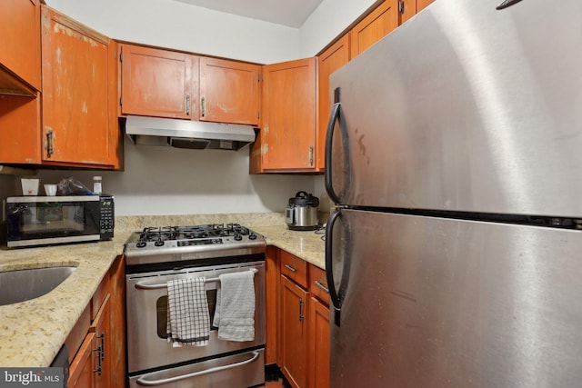 kitchen with stainless steel appliances, light stone counters, brown cabinetry, and under cabinet range hood