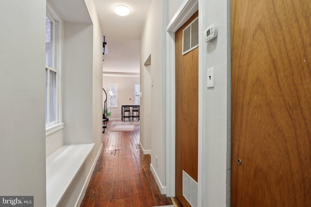 hallway with dark wood-style flooring, visible vents, and baseboards