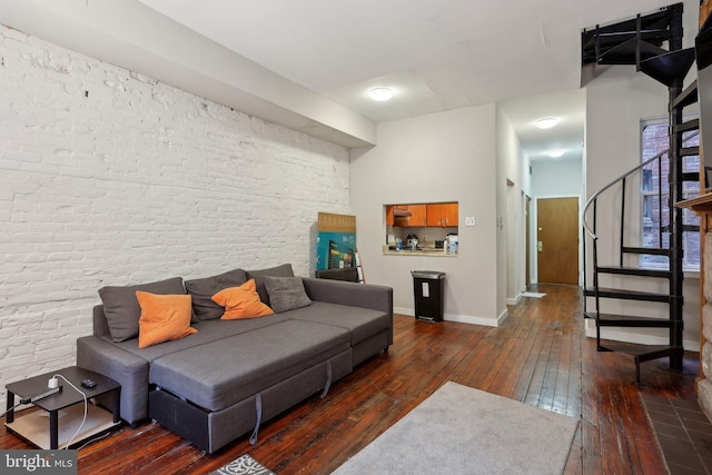 living room with wood-type flooring, baseboards, stairway, and brick wall