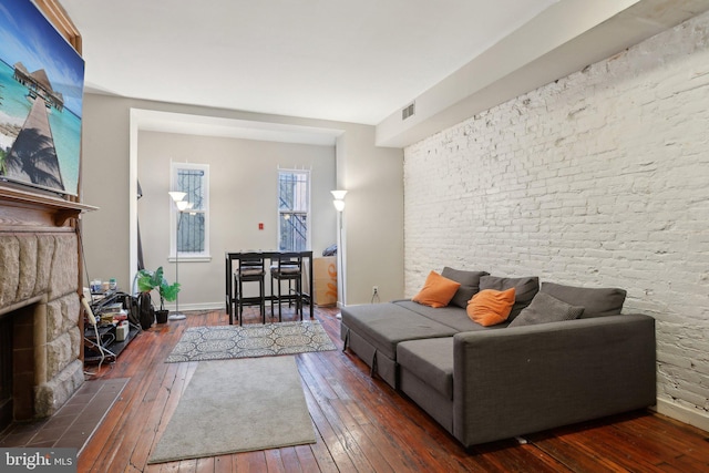 living room with visible vents, baseboards, brick wall, wood-type flooring, and a fireplace