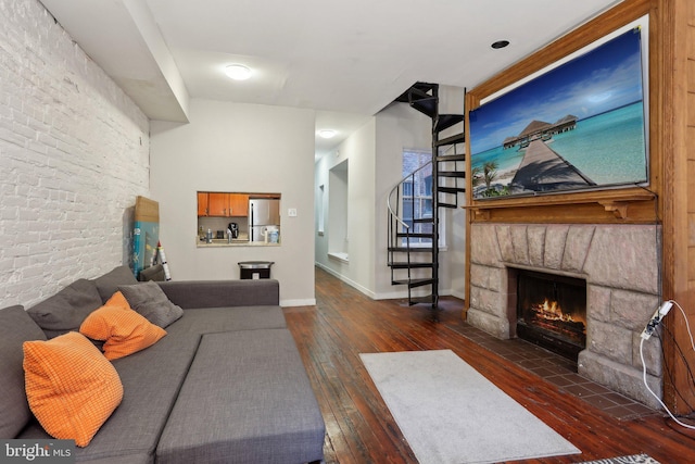 living room featuring hardwood / wood-style floors, a stone fireplace, brick wall, baseboards, and stairs