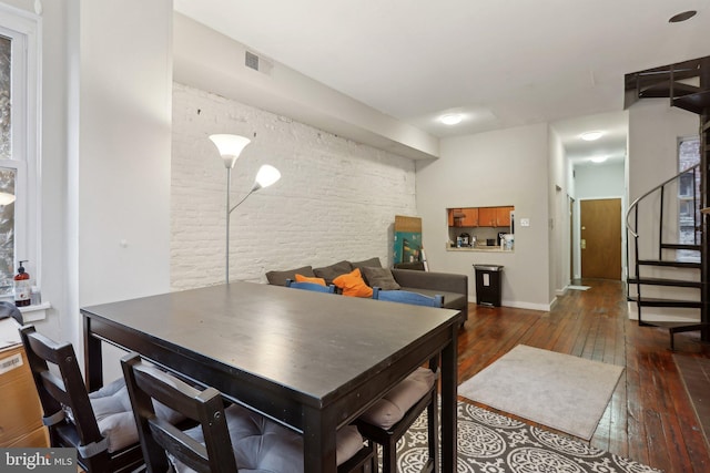 dining room with wood-type flooring, visible vents, stairway, and brick wall