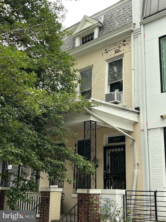 view of front facade featuring mansard roof, cooling unit, and brick siding